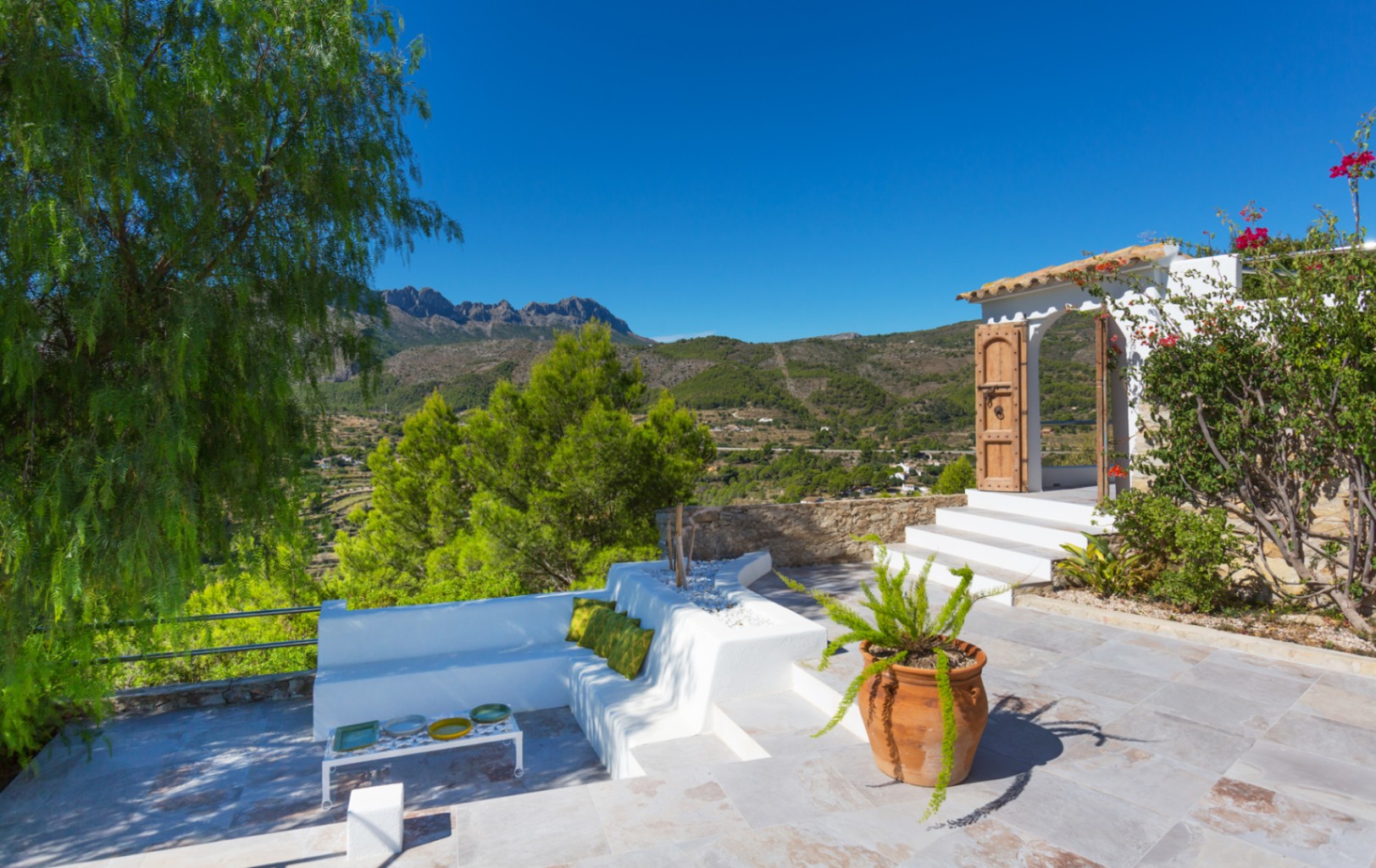Terraza con bancos de mampostería blanca, pavimentación de piedra y vistas panorámicas al paisaje montañoso y al valle.