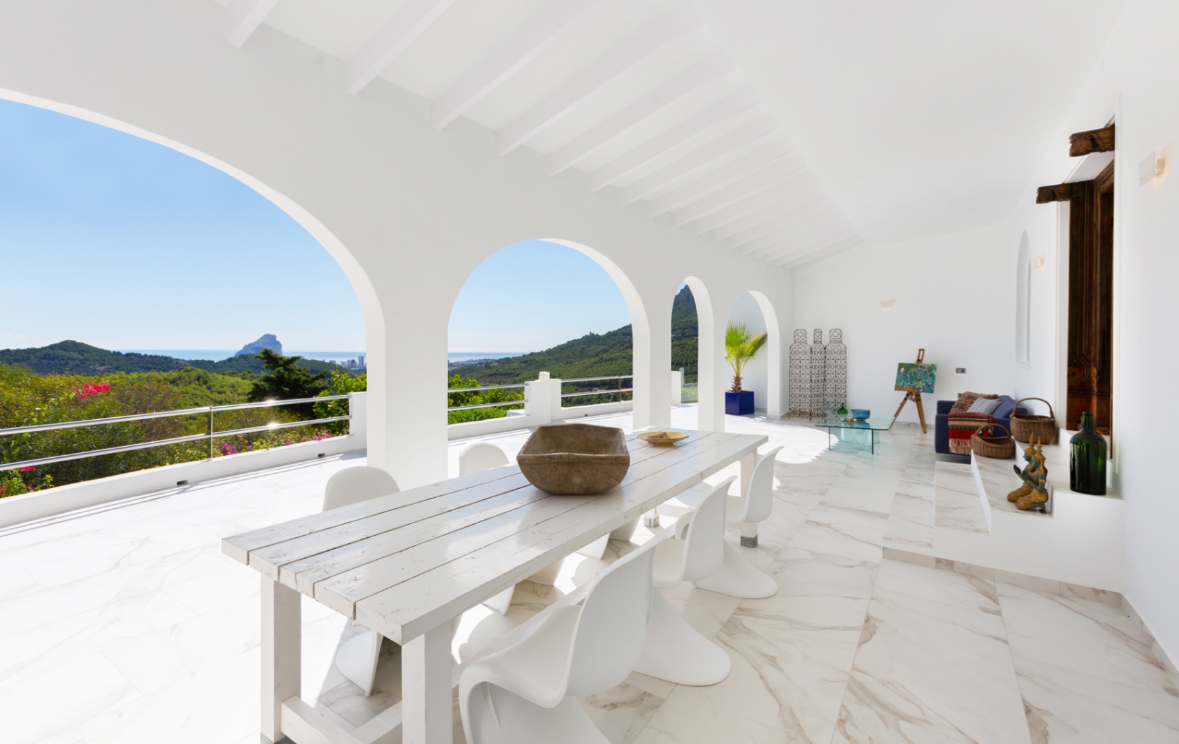 Terraza cubierta con arcos blancos, suelo de efecto mármol y comedor exterior con vistas panorámicas a la costa mediterránea y al Peñón de Ifach.