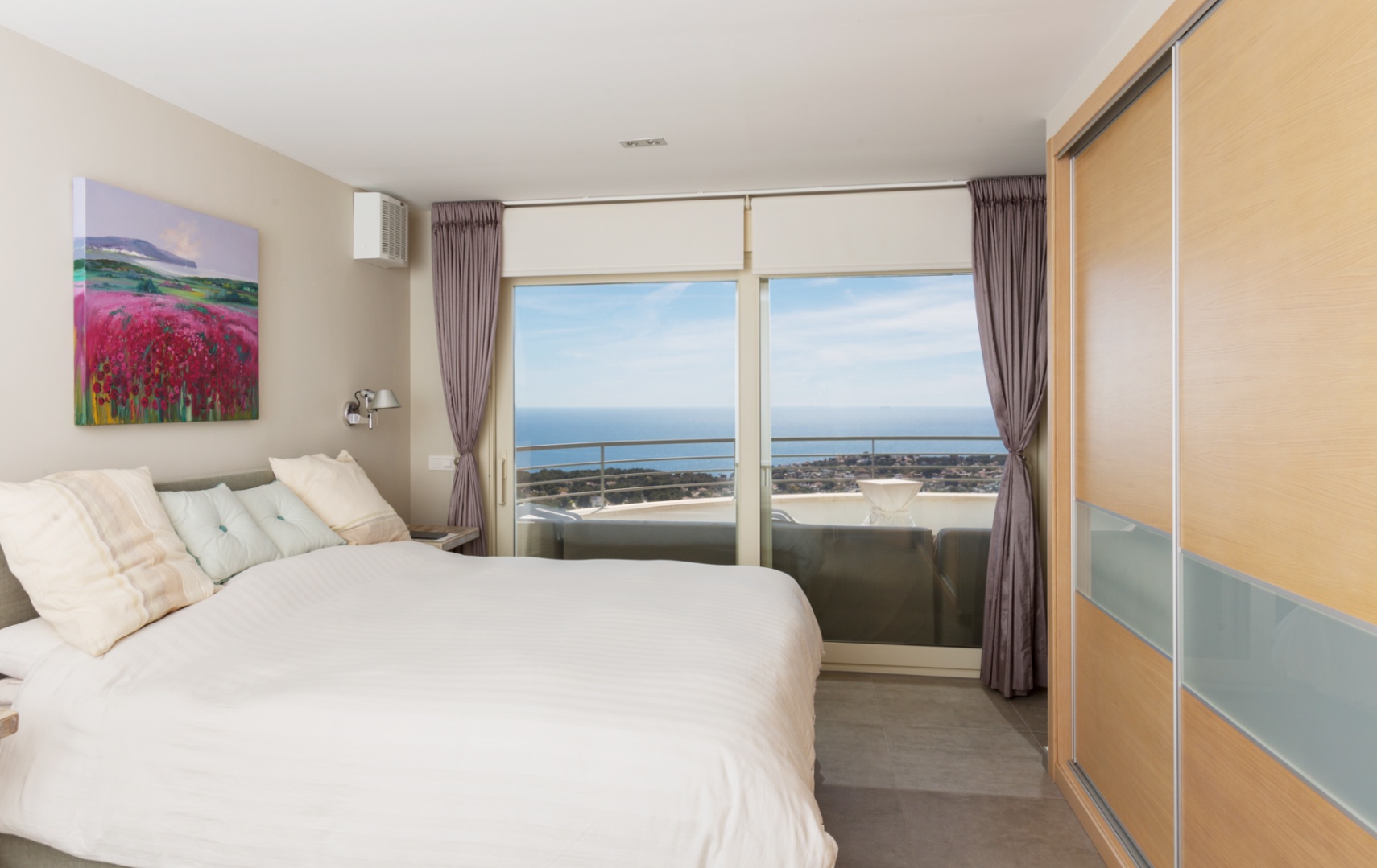 Dormitorio moderno con armario empotrado de madera y ventanales de suelo a techo que ofrecen vistas panorámicas al mar desde la terraza privada.