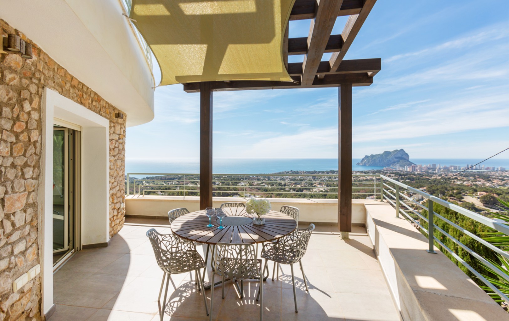 Terraza con muros de piedra natural, pérgola de madera y toldo vela. Incluye comedor exterior con vistas panorámicas al Mediterráneo y al Peñón de Ifach.