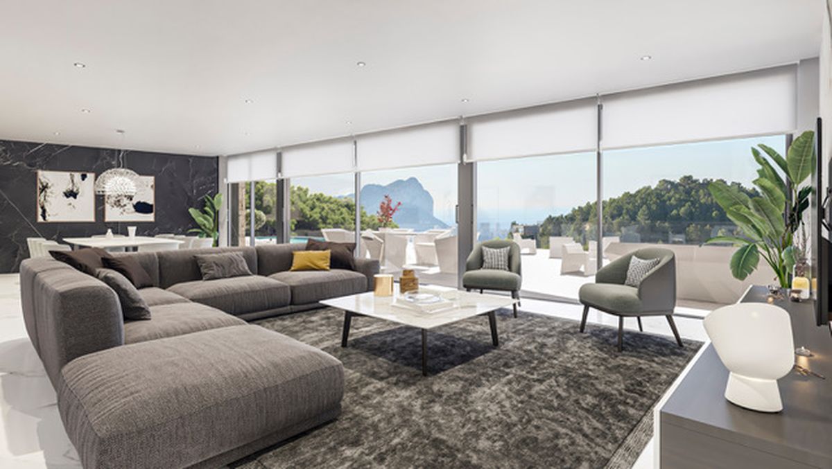 Amplio salón con sofá modular gris, mesa de mármol y ventanales de suelo a techo con vistas panorámicas al Peñón de Ifach y la costa mediterránea.