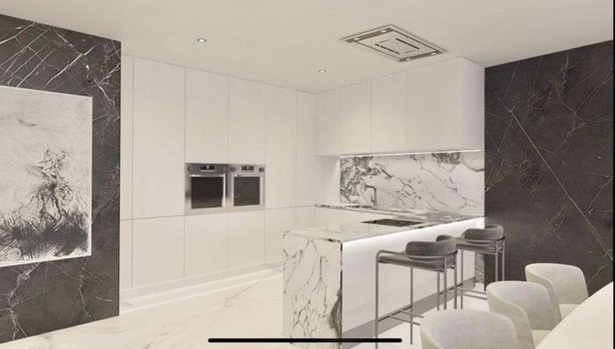 Cocina moderna con armarios blancos minimalistas, isla de mármol veteado, hornos dobles integrados y paneles de pared en mármol oscuro con iluminación técnica.