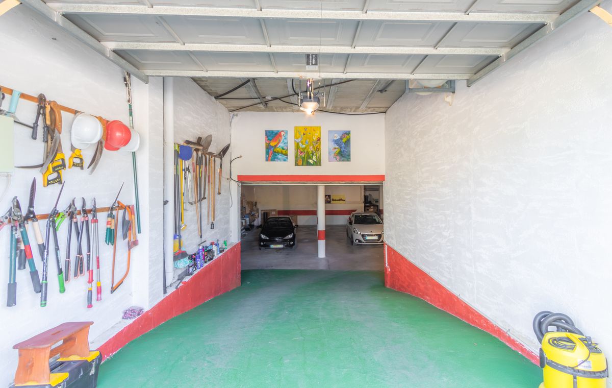 Amplio garaje con rampa de acceso verde, zona de herramientas organizada en paredes blancas y un nivel inferior con capacidad para varios vehículos.