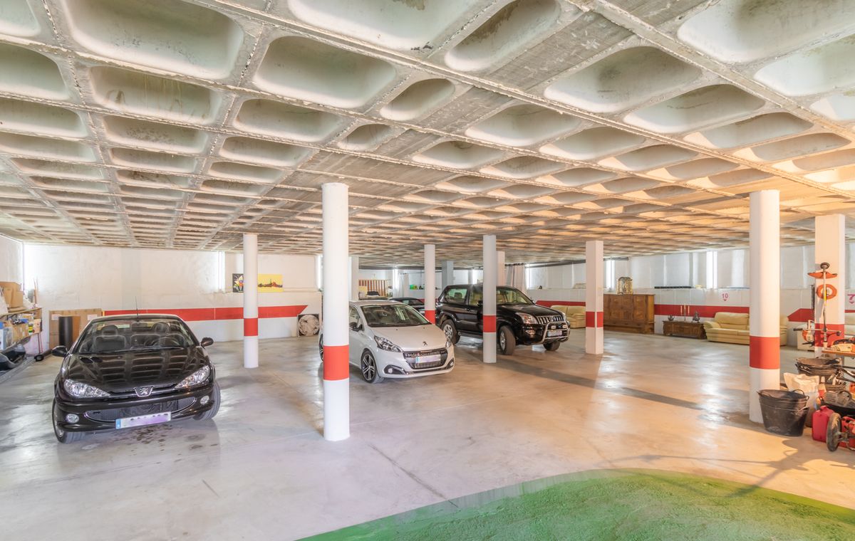 Amplio garaje subterráneo con un característico techo de forjado reticular de hormigón, columnas de soporte blancas con señalización roja y espacio para varios vehículos.