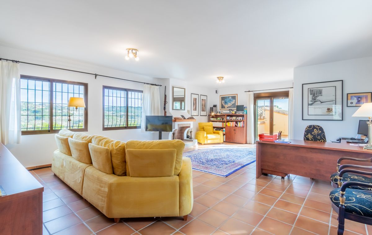 Amplio salón con suelo de terracota, sofá rinconero amarillo, zona de despacho con escritorio de madera y chimenea integrada.