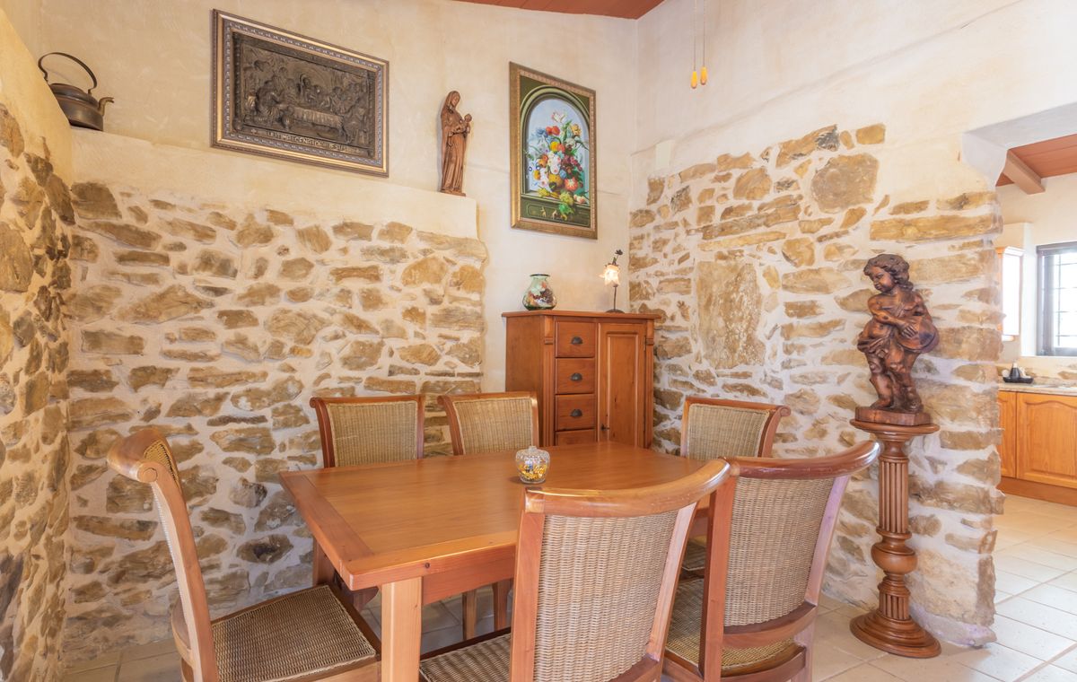 Comedor rústico con paredes de piedra natural vista, mesa de madera maciza con sillas de mimbre y elementos decorativos tradicionales de estilo clásico.