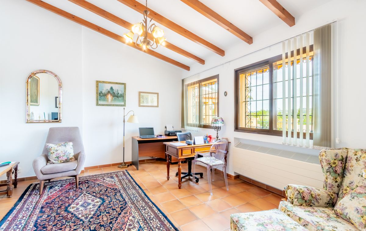 Despacho con vigas de madera a la vista, suelos de terracota y dos zonas de trabajo. Ventanales con rejas de seguridad aportan abundante luz natural.