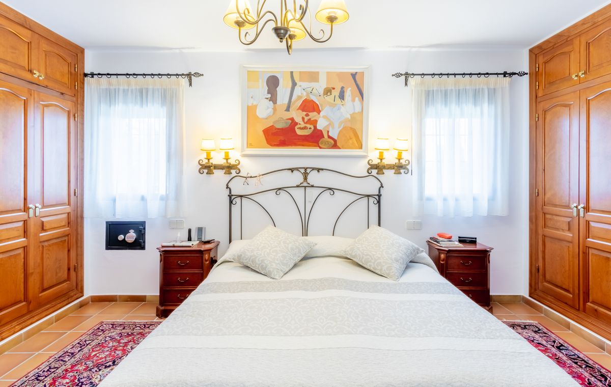 Dormitorio con cabecero de hierro forjado, armarios empotrados de madera simétricos y suelo de gres. Incluye apliques de pared y una caja fuerte integrada.