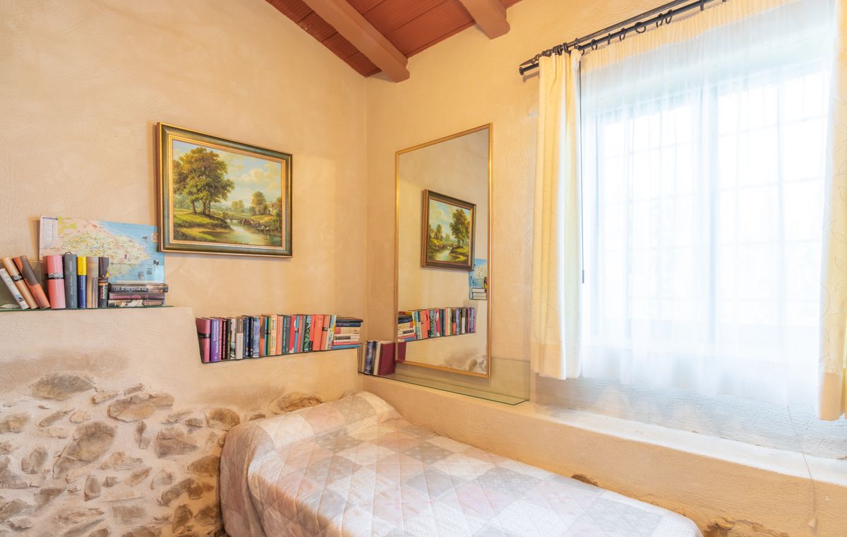 Dormitorio pequeño con cama individual, vigas de madera a la vista y detalle de pared en piedra natural. Incluye estantes de cristal integrados y un gran espejo vertical.