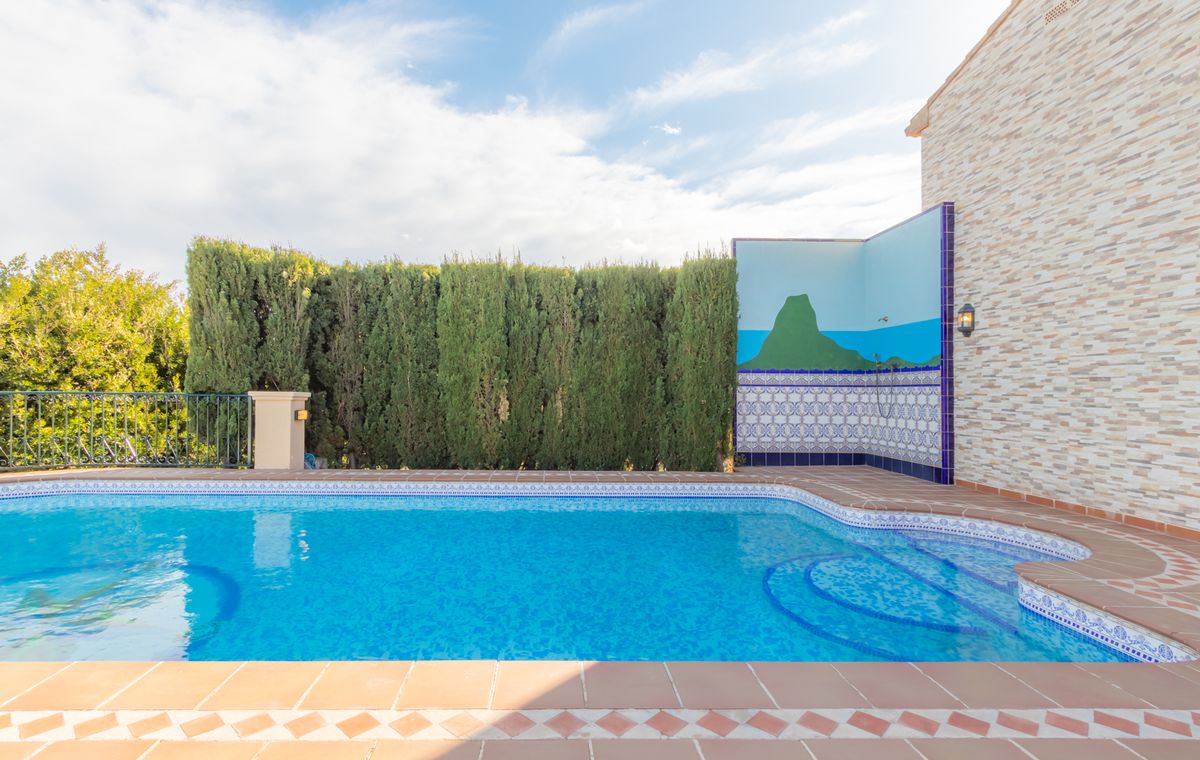 Piscina exterior con escalones curvos, borde de terracota y zona de ducha privada decorada con un mural paisajístico y azulejos tradicionales.