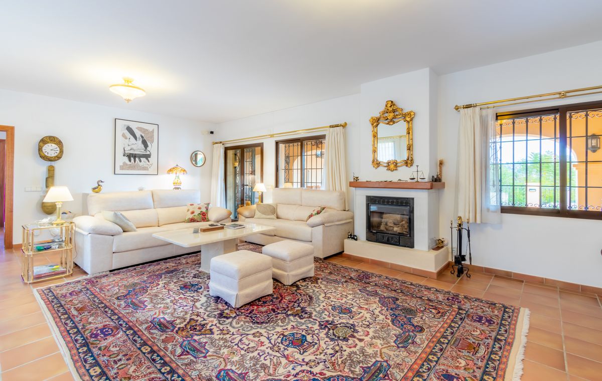 Salón espacioso con suelos de terracota, chimenea con espejo de marco dorado y sofás blancos dispuestos sobre una gran alfombra de diseño tradicional.