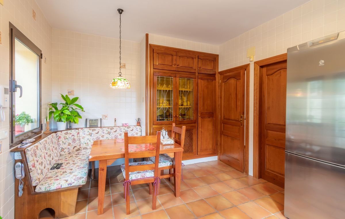 Zona de comedor en cocina con banco de madera rinconero, suelos de terracota y armarios empotrados de madera con vitrinas de cristal.
