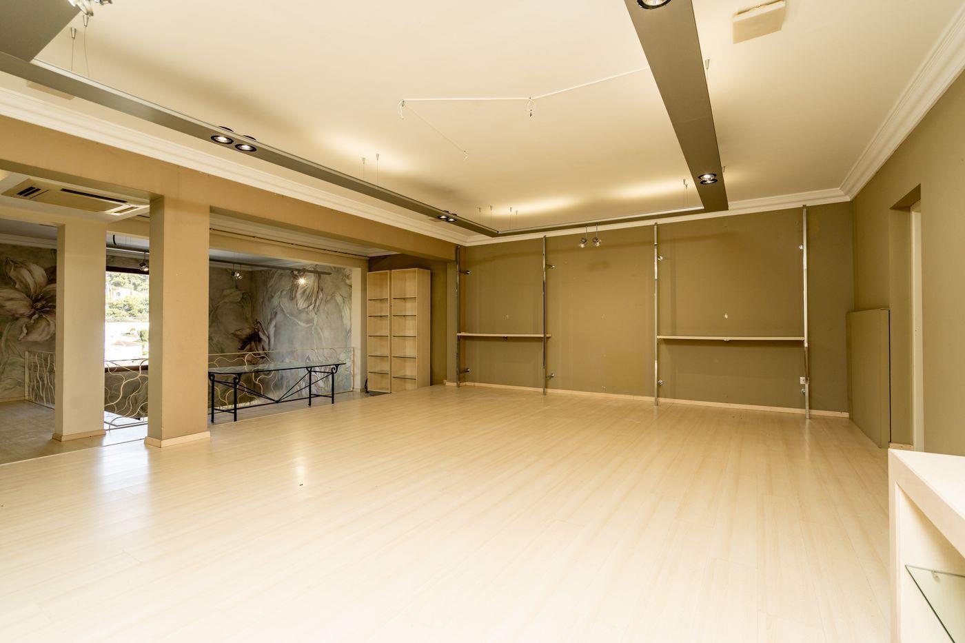 Amplia sala diáfana con suelos de laminado claro, iluminación técnica en rieles de techo y estanterías metálicas modulares en paredes de tono arena.