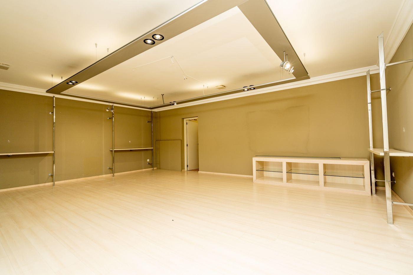 Amplio espacio con suelo de madera clara, techo técnico con iluminación integrada y estanterías metálicas de diseño sobre paredes en tono oliva.