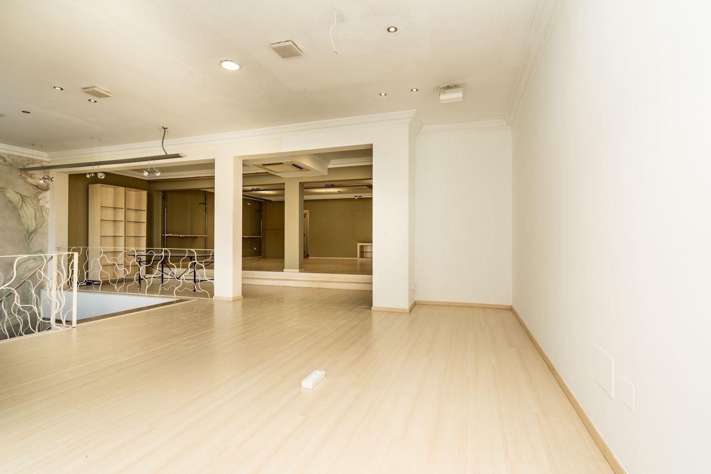 Amplio espacio diáfano con suelos de madera clara, iluminación empotrada y una barandilla decorativa de metal blanco que asoma al nivel inferior.