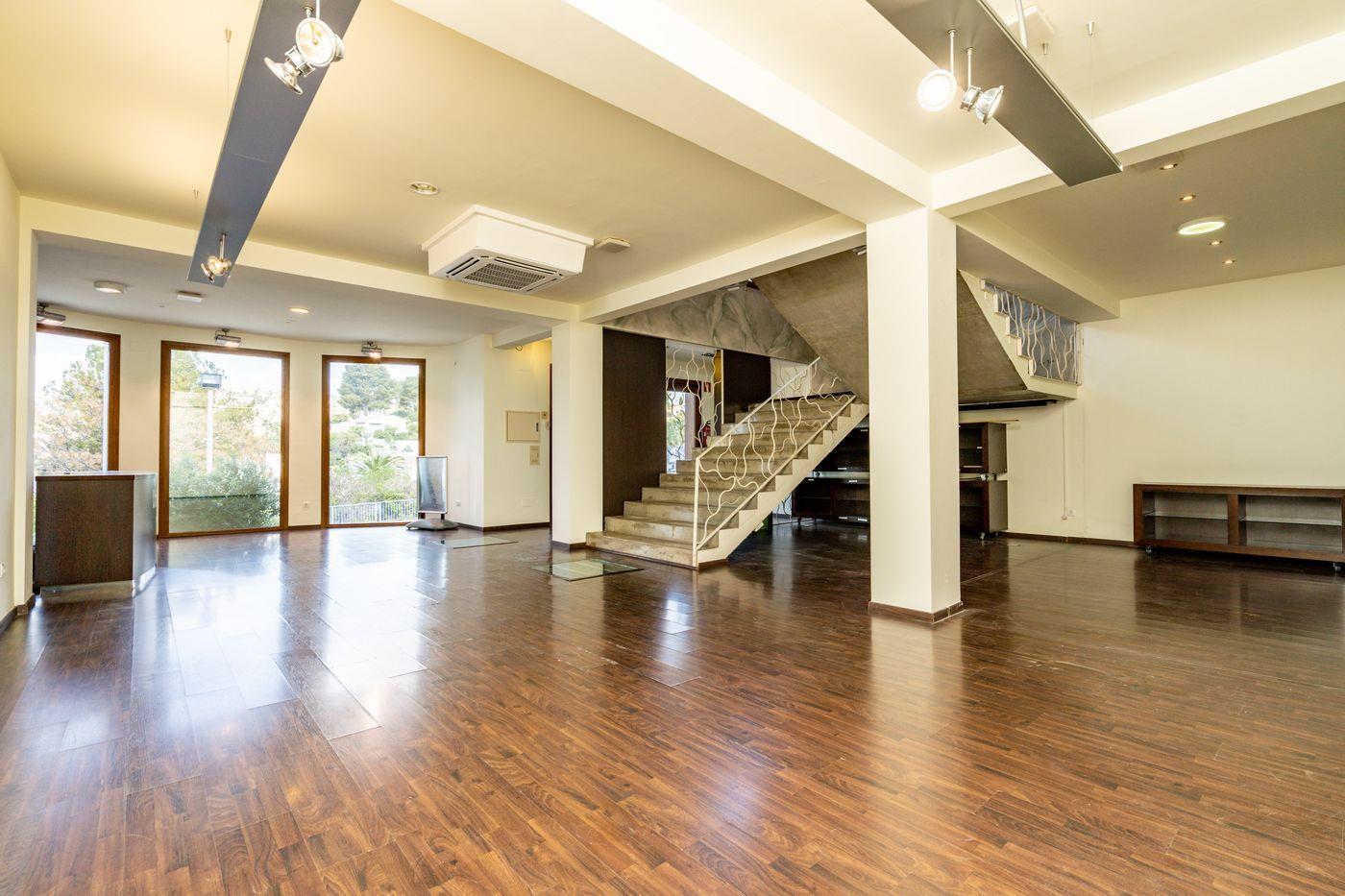 Amplio interior diáfano con suelos de madera oscura, una escalera central de hormigón con barandilla decorativa blanca e iluminación técnica integrada.