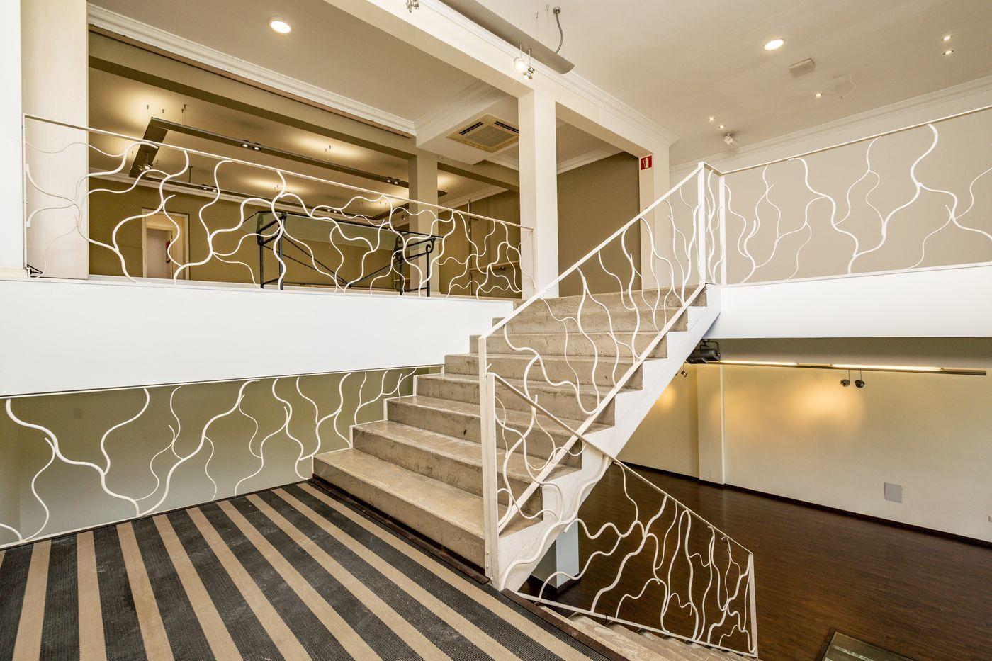 Escalera interior moderna con peldaños de piedra y una barandilla metálica blanca de diseño orgánico, que conecta la planta baja con el entresuelo.