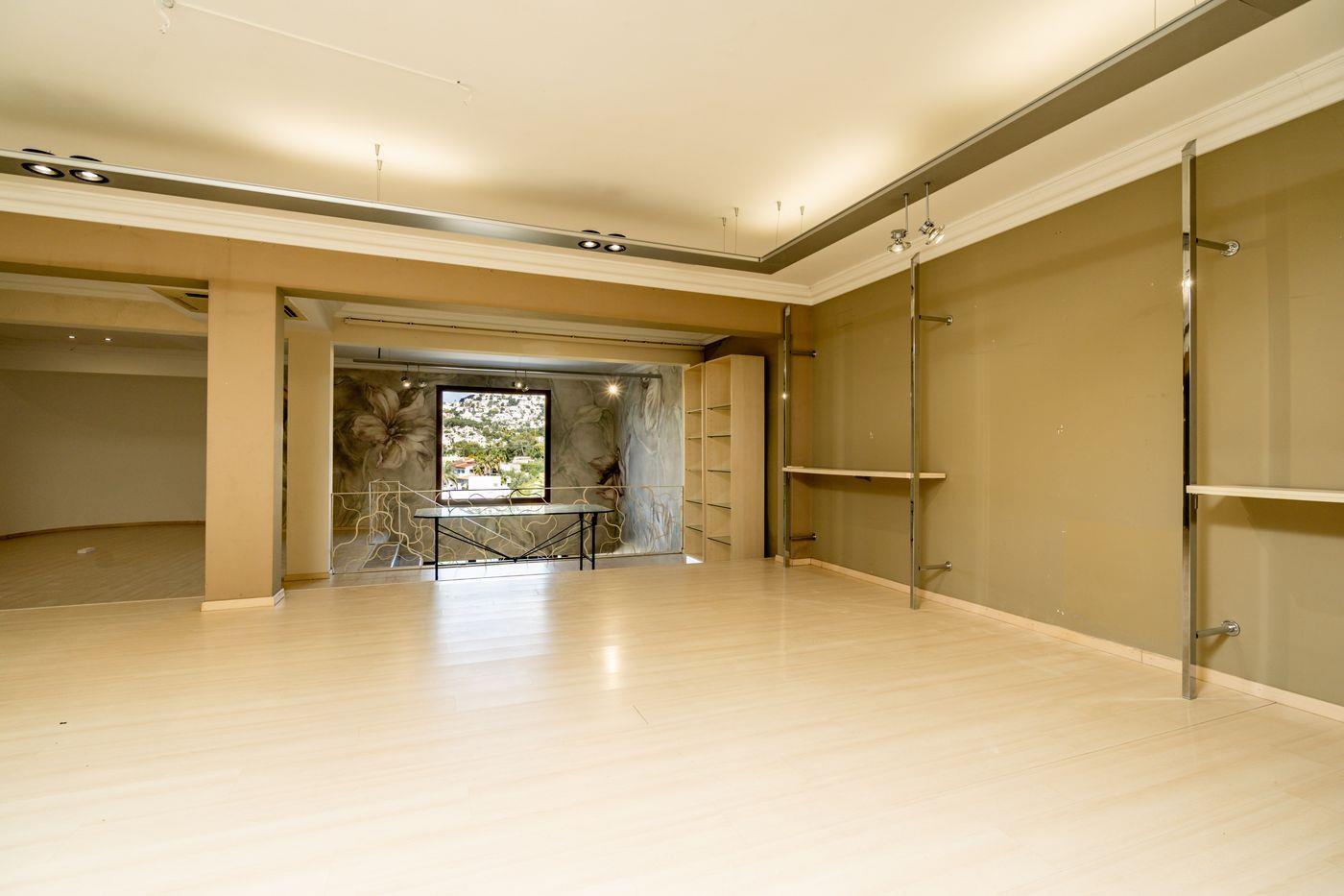 Espacio diáfano con suelos de madera clara, iluminación técnica integrada y estructuras metálicas. Un gran ventanal ofrece vistas despejadas a la colina.