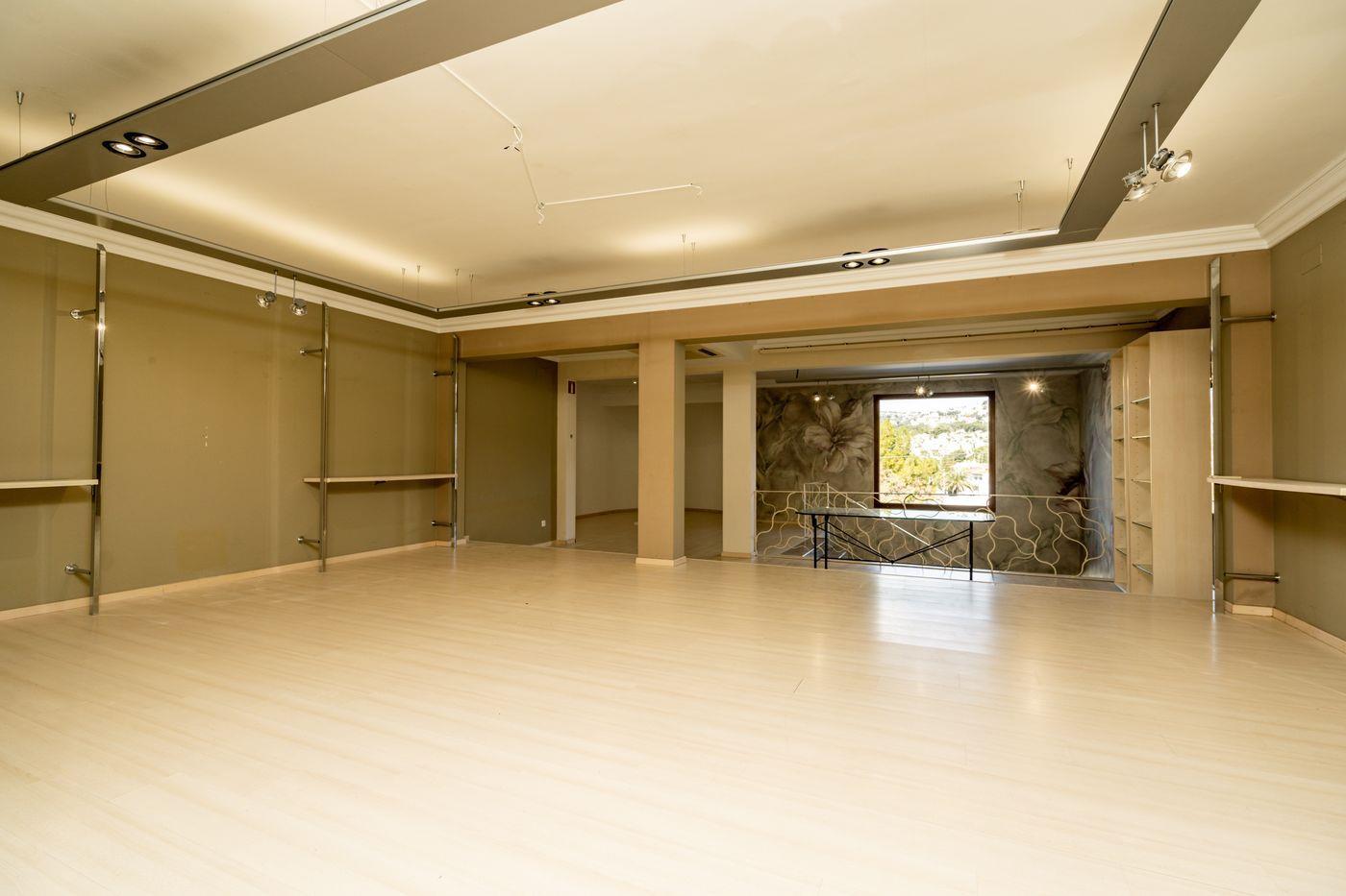 Local comercial diáfano con suelos de laminado claro, estanterías metálicas modulares y un mural floral decorativo junto a un ventanal con vistas al exterior.