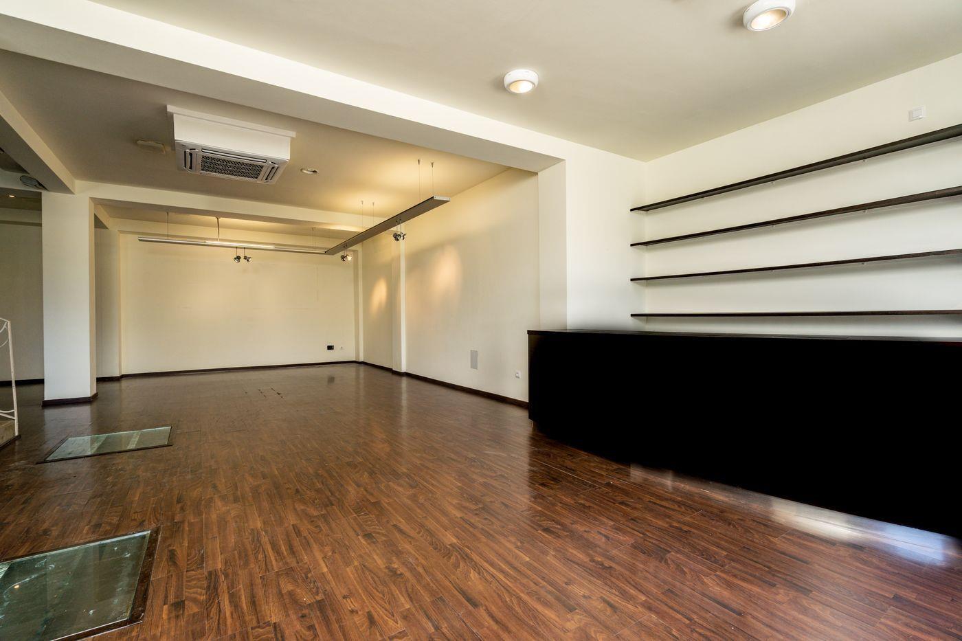Local comercial diáfano con suelos de madera oscura, mostrador negro con estanterías a juego y climatización por conductos en el techo.