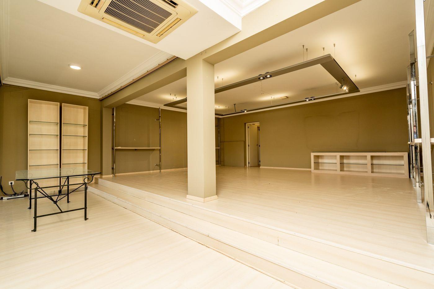 Local comercial diáfano con suelos laminados en dos niveles, aire acondicionado por conductos y sistema de iluminación técnica sobre una zona de exposición elevada.