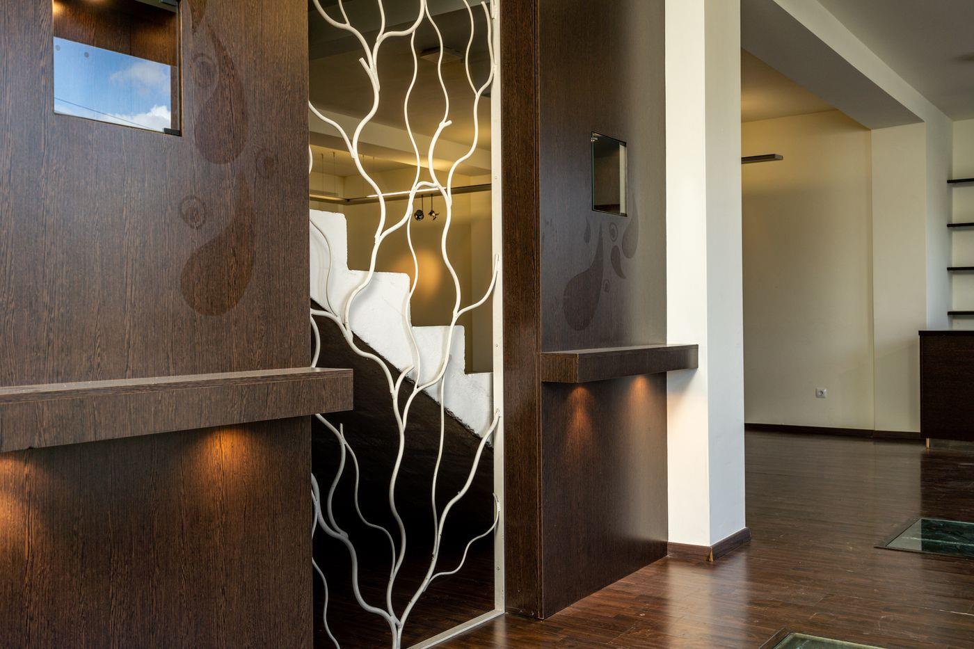 Pasillo de entrada con paneles de madera oscura, iluminación integrada y un separador metálico blanco con diseño orgánico de ramas frente a la escalera.