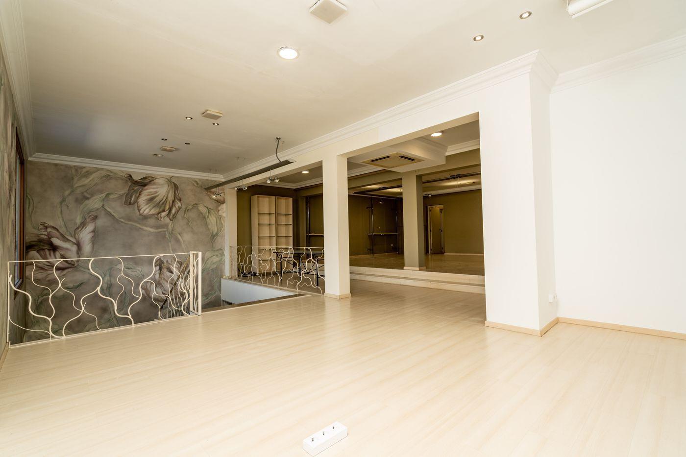 Planta superior diáfana con suelos de madera clara, iluminación empotrada y una barandilla metálica decorativa. Destaca el mural floral artístico en la pared lateral.