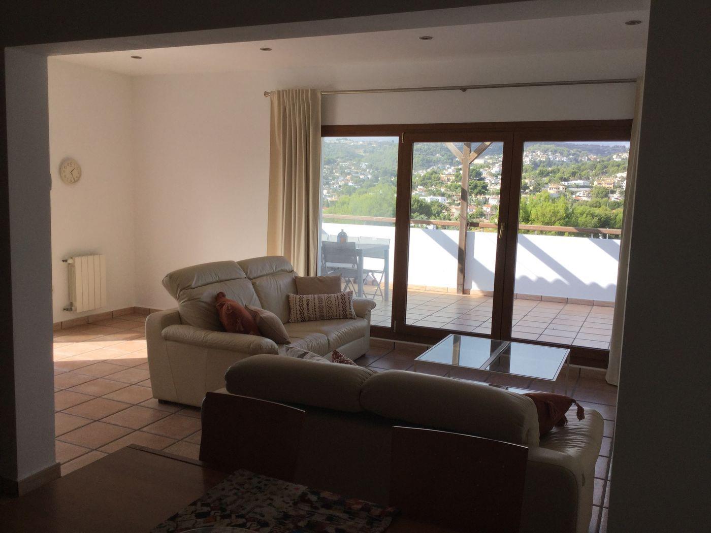Salón con sofás de cuero crema, suelo de baldosas de terracota y grandes puertas correderas de madera con acceso a una terraza con vistas despejadas.