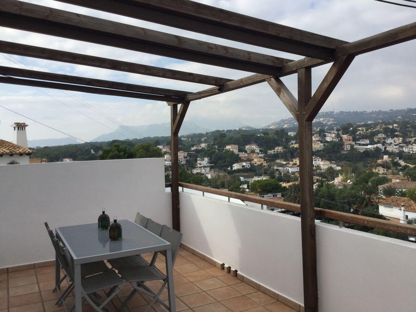 Terraza con pérgola de madera, suelo de terracota y conjunto de comedor exterior con vistas despejadas al valle y las montañas circundantes.