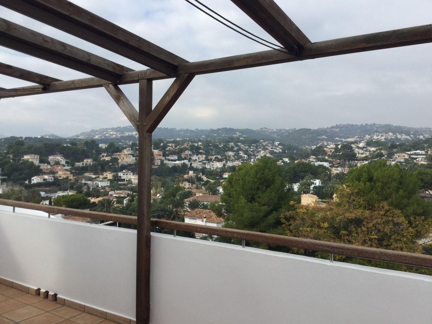 Terraza elevada con pérgola de madera oscura y barandilla, ofreciendo vistas panorámicas a un valle residencial con vegetación mediterránea.
