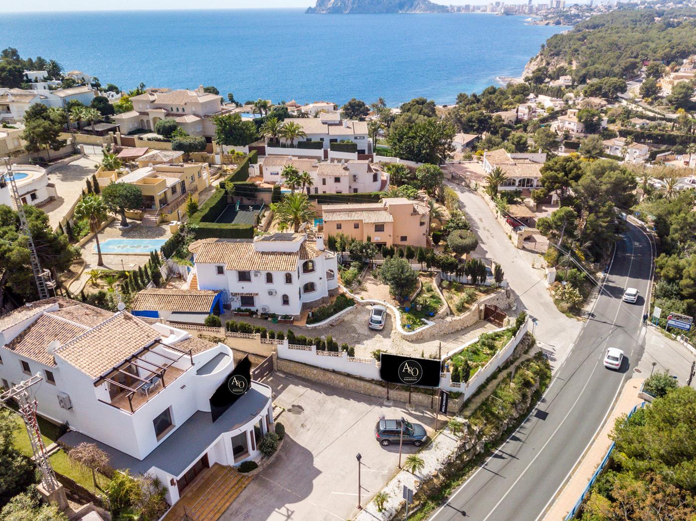 Vista aérea de una villa blanca con tejado de arcilla, situada junto a la carretera costera con vistas panorámicas al mar Mediterráneo y al entorno residencial.
