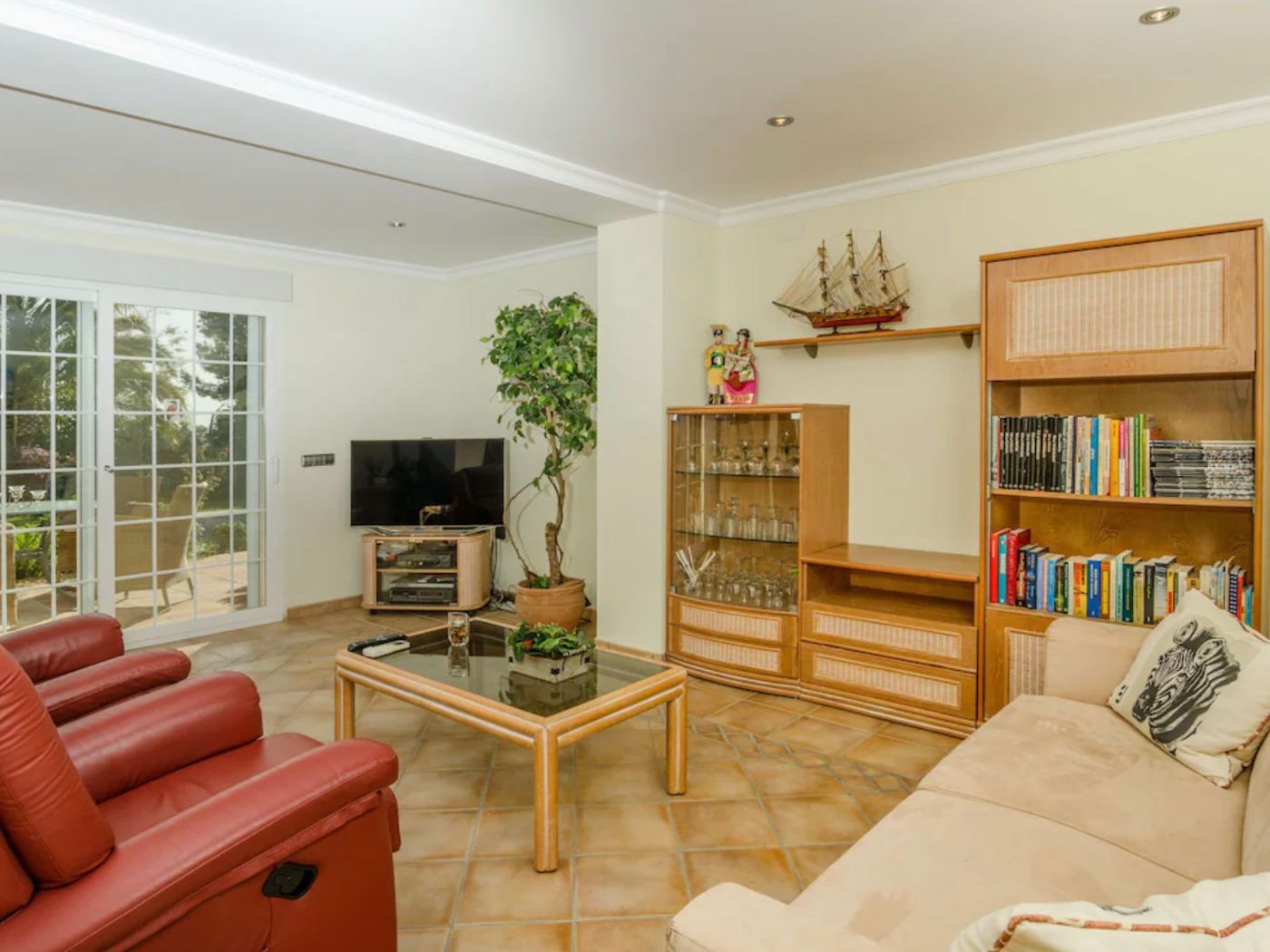 Salón con suelos de terracota, sofás de cuero rojo y muebles de madera clásicos. Incluye acceso directo a la terraza mediante puertas correderas acristaladas.