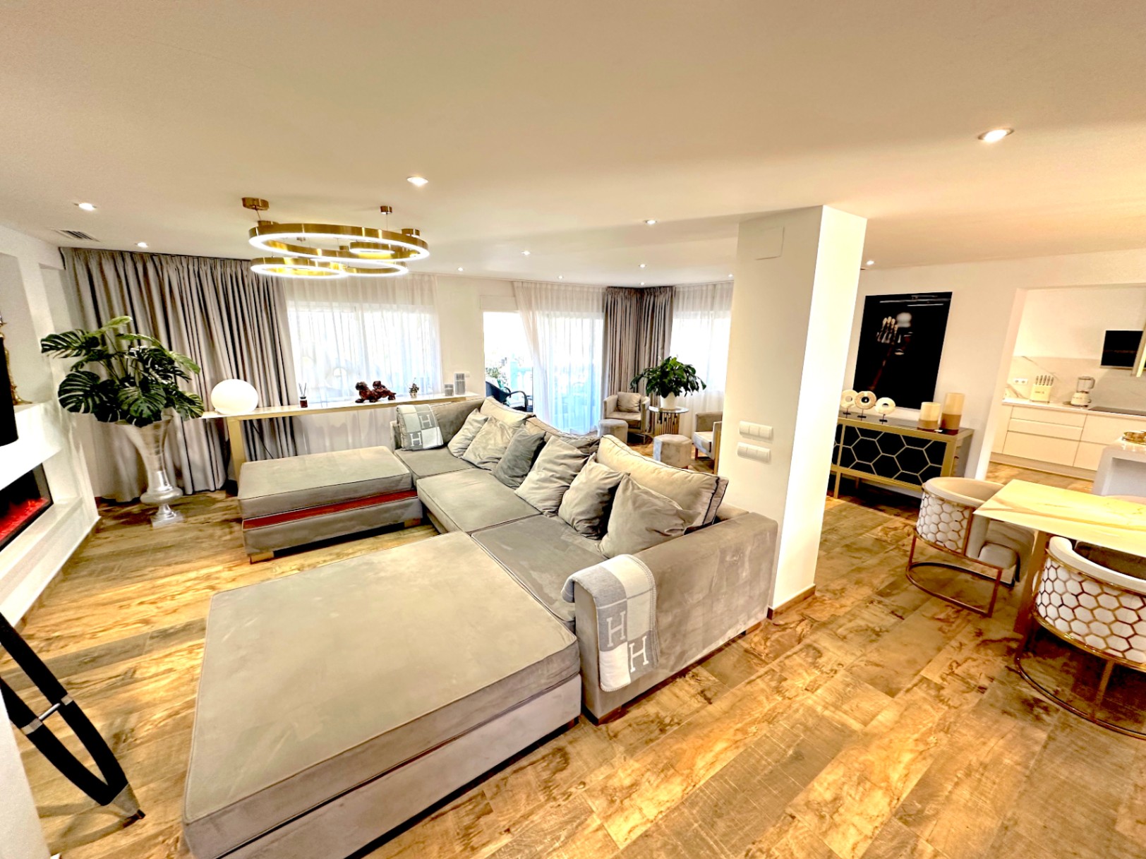 Salón de concepto abierto con suelos de madera, gran sofá modular gris, chimenea lineal y una lámpara circular dorada de diseño contemporáneo.