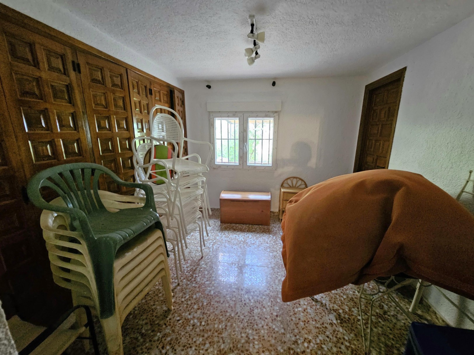 Habitación con armarios empotrados de madera tallada, suelo de terrazo y ventana con rejas. Espacio funcional con gran capacidad de almacenamiento.