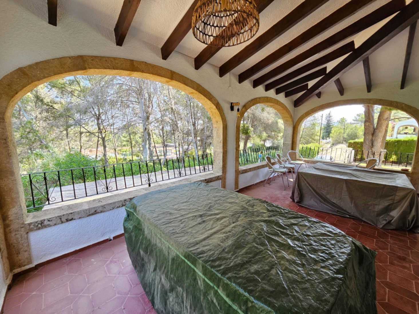 Terraza cubierta con arcos de piedra tosca, vigas de madera a la vista y suelo de baldosas hexagonales con vistas al bosque de pinos.