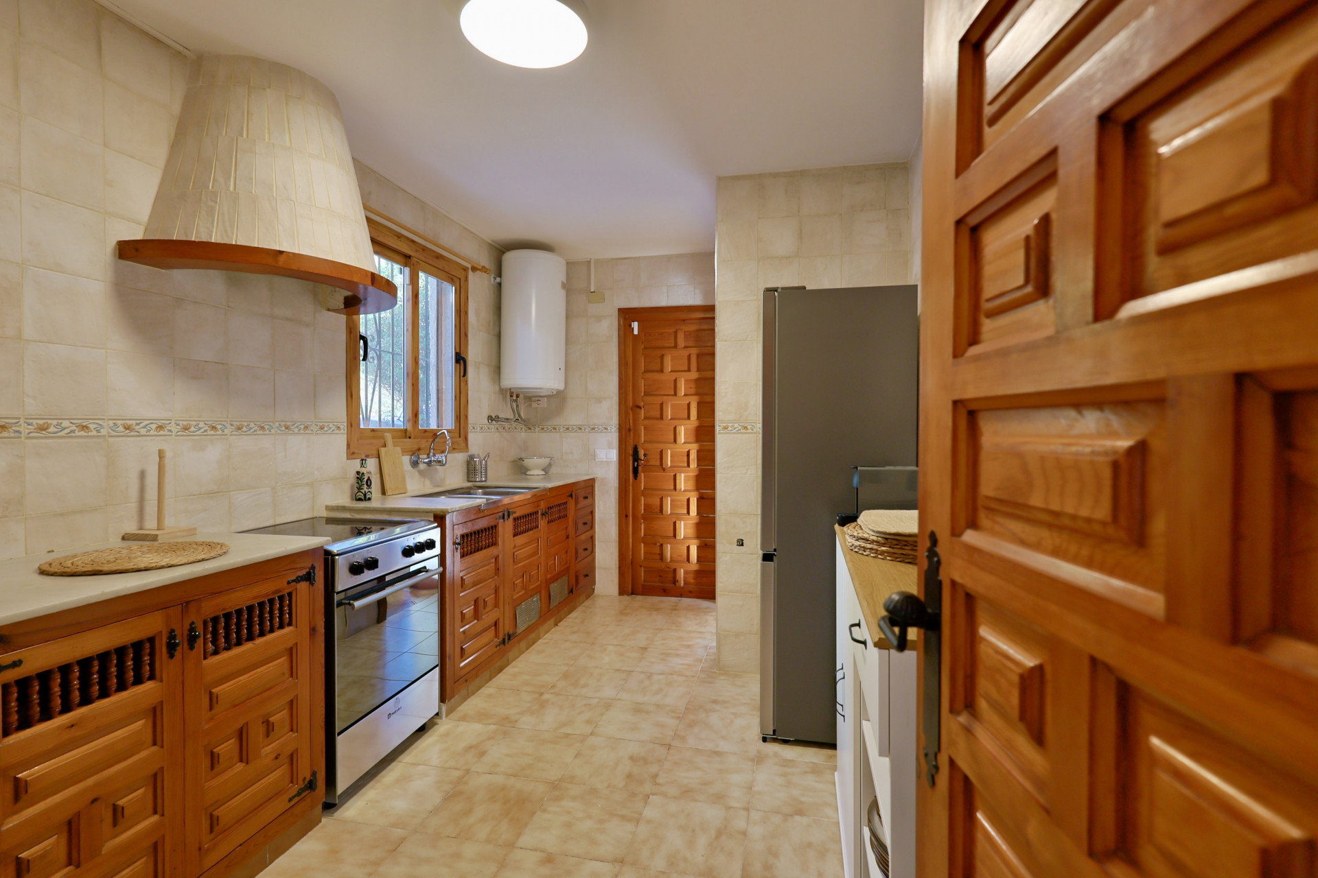 Cocina de estilo rústico con armarios de madera tallada, campana extractora cónica revestida de azulejos y electrodomésticos de acero inoxidable.