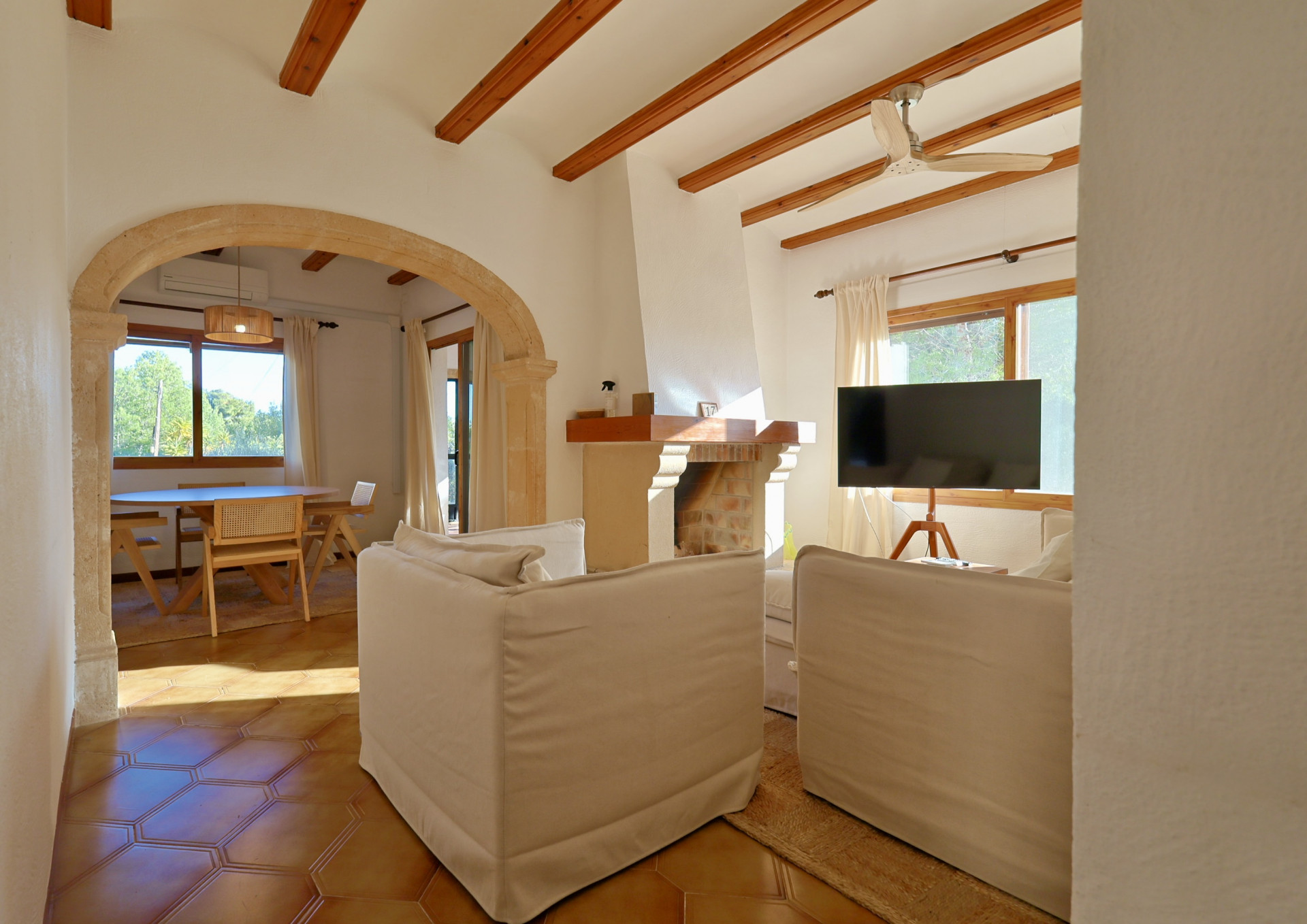 Salón con vigas de madera vistas, un arco de piedra natural y suelos de terracota. Cuenta con chimenea tradicional y acceso directo al comedor luminoso.