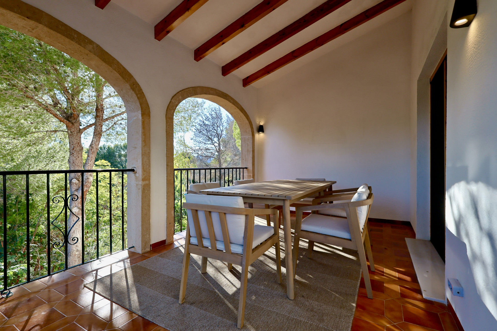 Terraza cubierta con arcos de piedra tosca, vigas de madera a la vista y suelo de barro cocido. Incluye un comedor exterior con vistas al entorno arbolado.