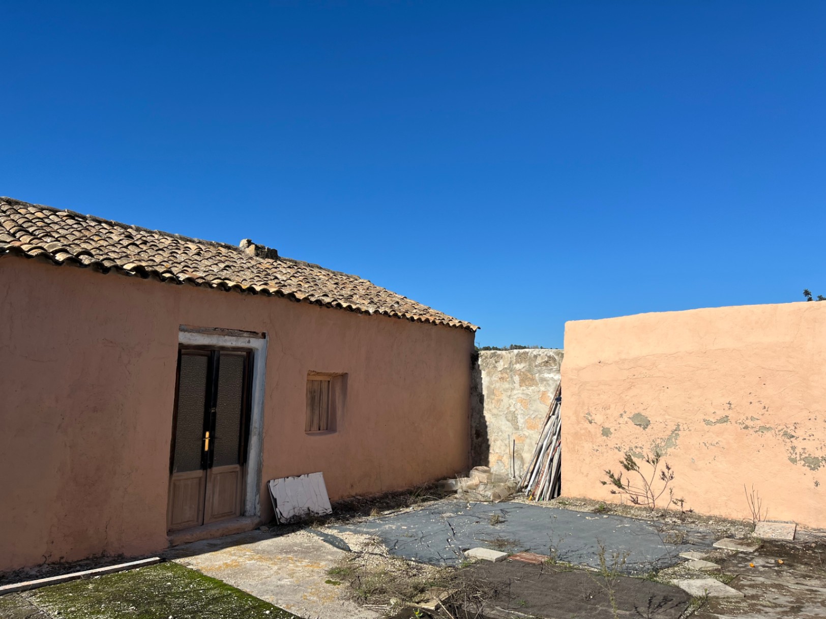 Fachada exterior de una finca tradicional con paredes de color terracota, tejado de teja árabe y puerta de madera, lista para una reforma integral.