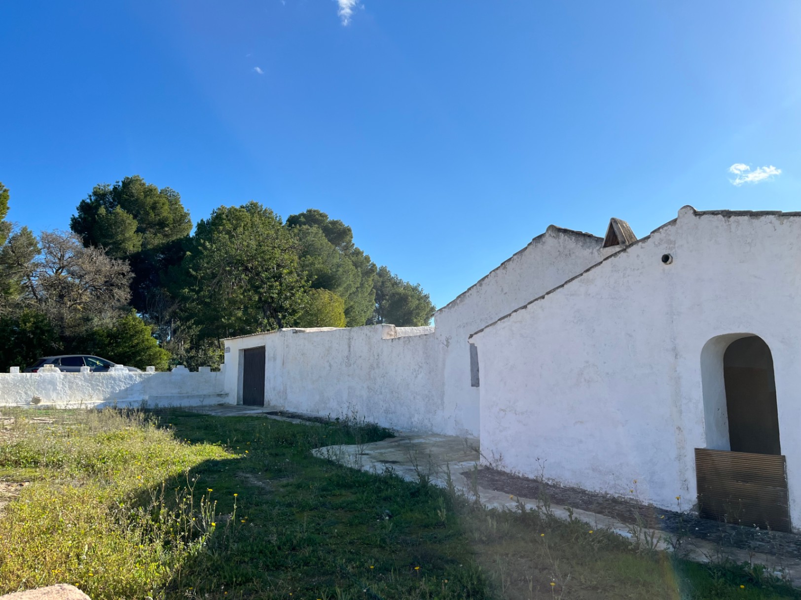 Fachada exterior de una finca tradicional en Jávea con muros de piedra encalados, entrada en arco y vegetación mediterránea bajo un cielo despejado.
