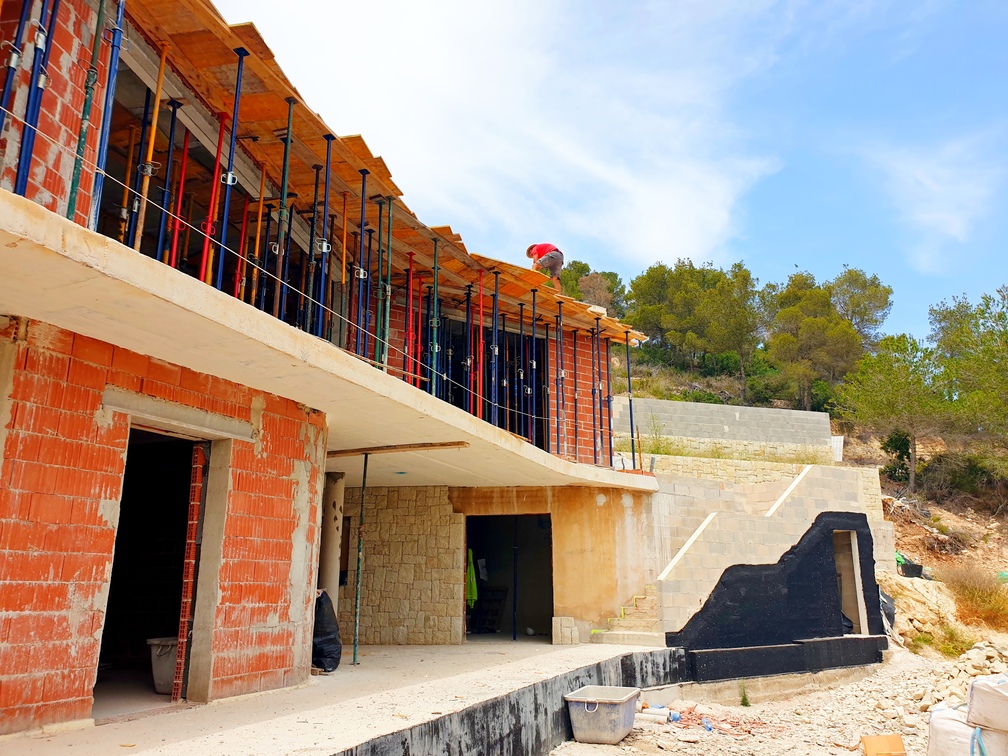 Chalet moderno en construcción con muros de ladrillo cerámico, forjados de hormigón y puntales. Destaca el revestimiento de piedra natural y la escalera exterior en proceso.