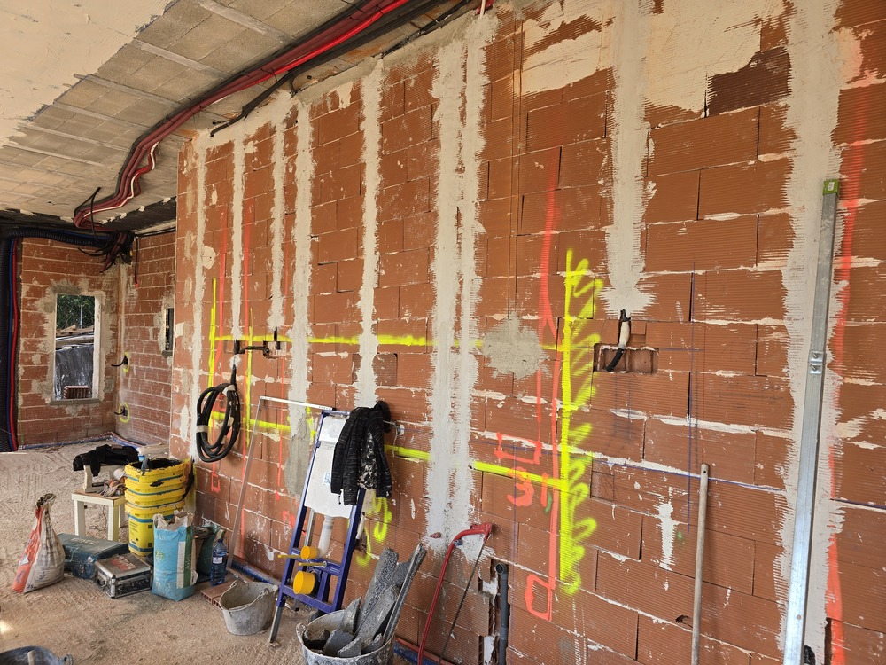 Fase de construcción que muestra un muro de ladrillo cerámico con marcas fluorescentes para instalaciones eléctricas y conductos vistos en el techo.