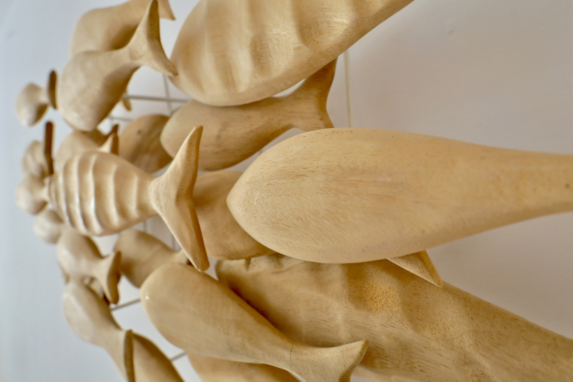 Primer plano de una escultura decorativa de pared con peces de madera tallados a mano en diversas texturas, montados sobre una estructura metálica minimalista.