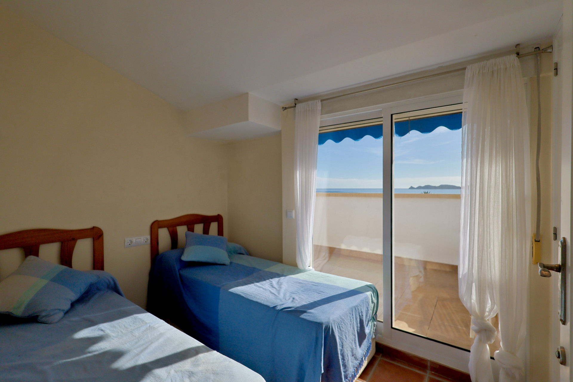 Dormitorio con dos camas individuales, cabeceros de madera y acceso directo a una terraza con vistas despejadas al mar Mediterráneo.