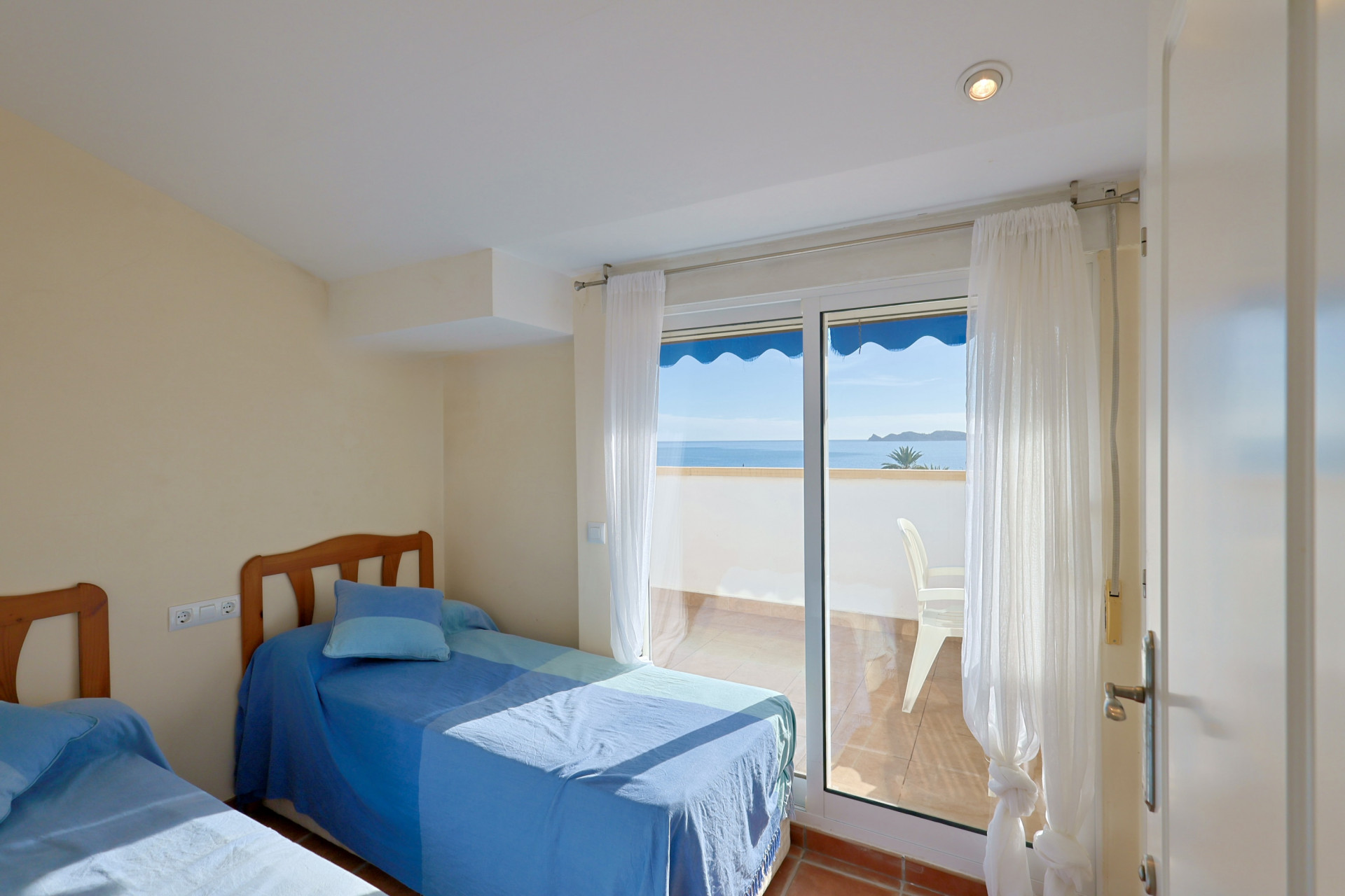 Dormitorio con dos camas individuales y cabeceros de madera, con acceso directo a una terraza privada con vistas al mar Mediterráneo.