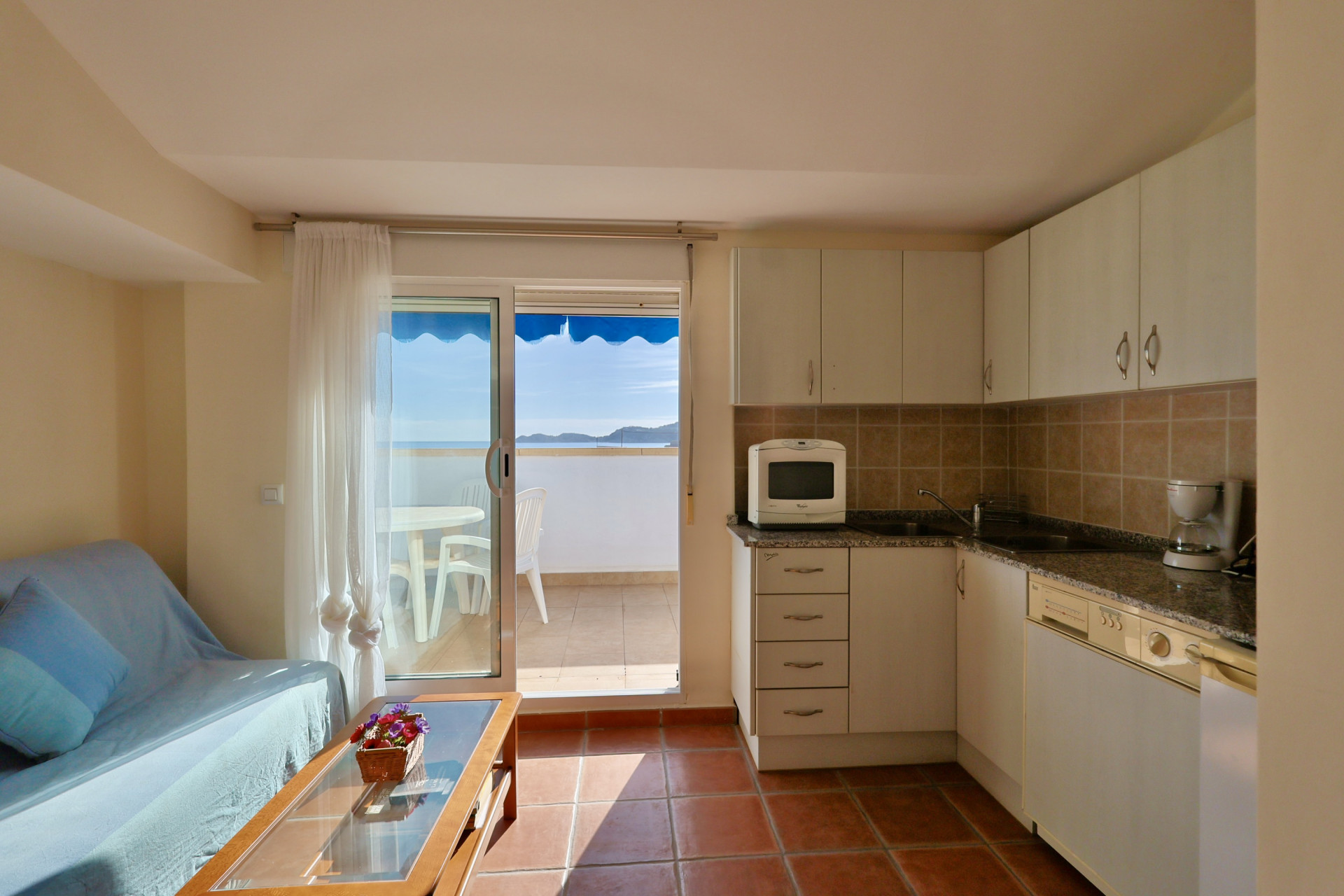 Zona de estar abierta con cocina compacta, encimeras de granito y acceso directo a una terraza privada con vistas panorámicas al mar Mediterráneo.