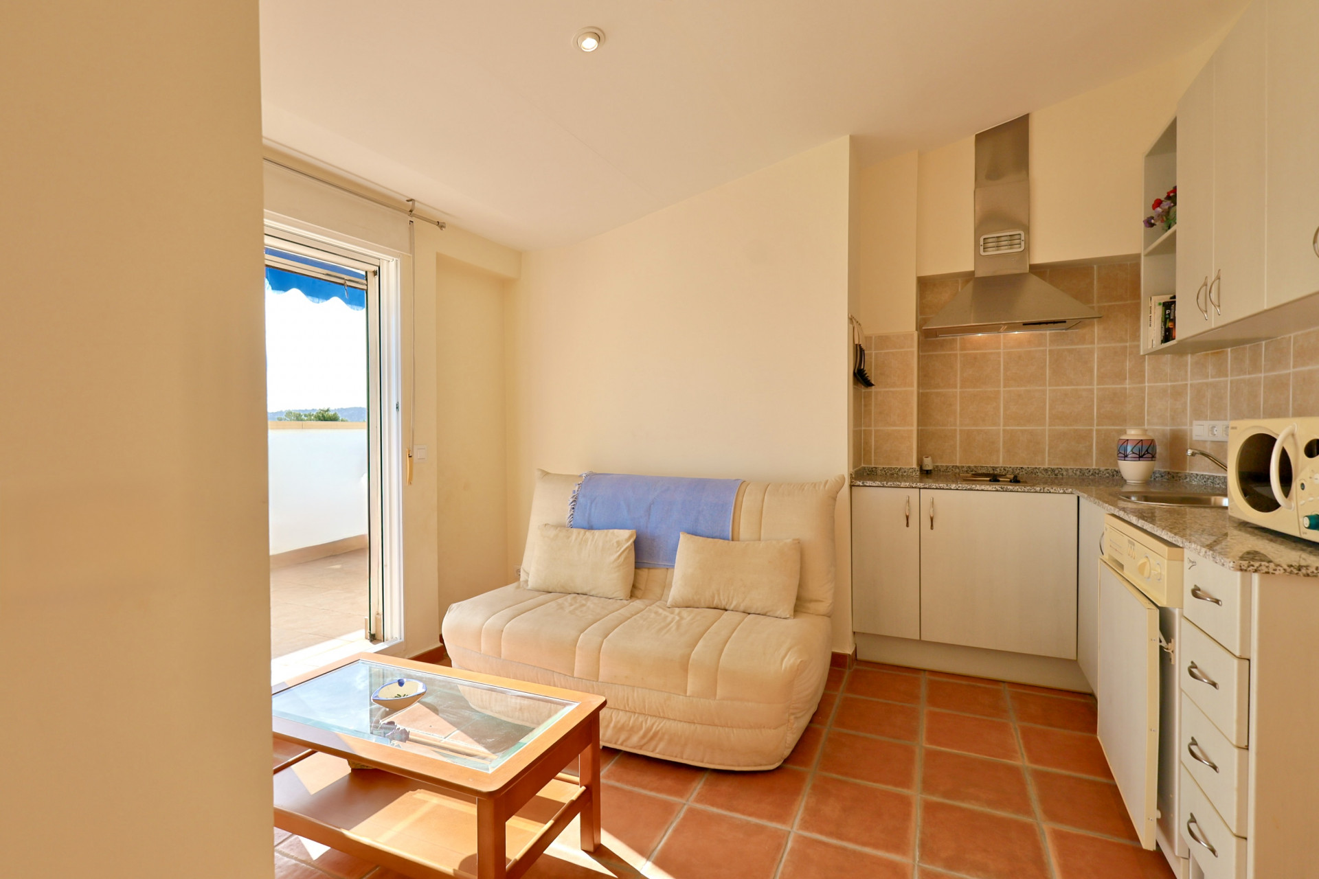 Zona de estar de planta abierta con suelos de terracota, cocina compacta con encimeras de granito y acceso a la terraza exterior mediante puertas correderas.