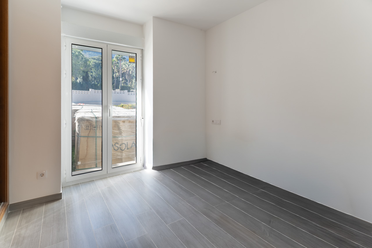 Habitación vacía con suelo de gres porcelánico gris y acceso directo al exterior mediante puerta acristalada de PVC blanco.