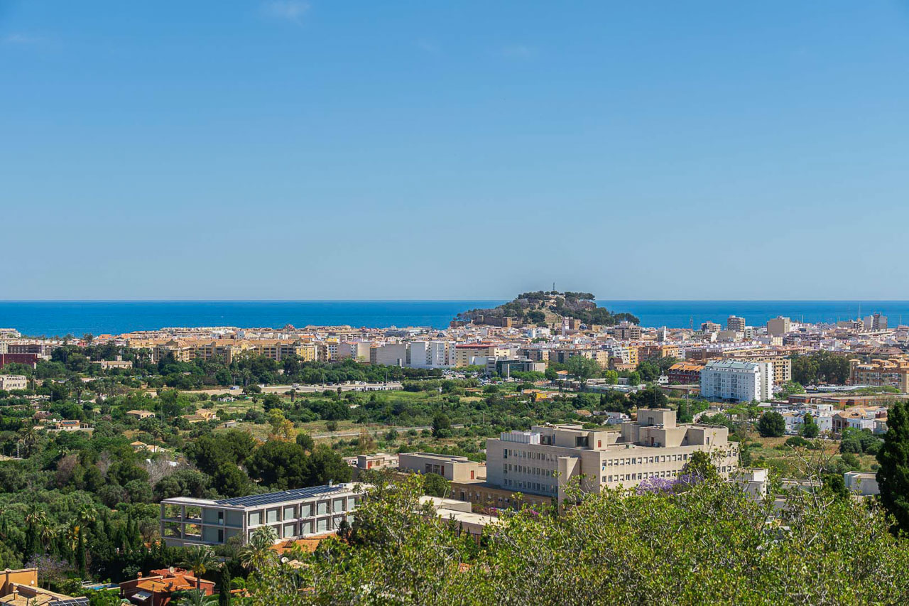 Vistas panorámicas de la ciudad costera con el castillo sobre la colina, arquitectura urbana diversa y el mar Mediterráneo bajo un cielo despejado.
