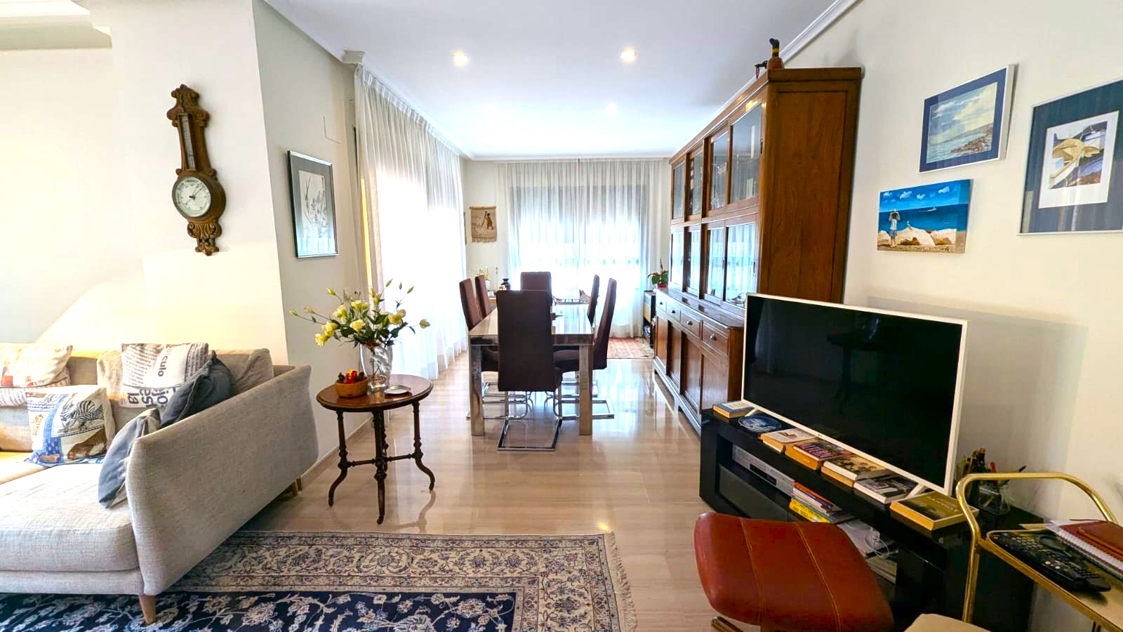 Amplio salón-comedor con suelos de mármol pulido, una gran vitrina de madera clásica y mesa de comedor de cristal bajo iluminación de focos empotrados.